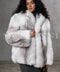 A woman wears a meticulously handcrafted full-pelt Arctic fox fur coat, featuring exceptional softness, volume, and a loose fit with a plush hood that envelops her in luxurious warmth and elegant style.