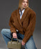 Stylishly dressed, a woman models a supple brown suede jacket featuring bold shoulders and a chic cropped silhouette.