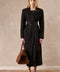 A woman wears a long dark brown suede coat with wide shoulders and a cinched belt, showcasing timeless elegance and strong tailoring.